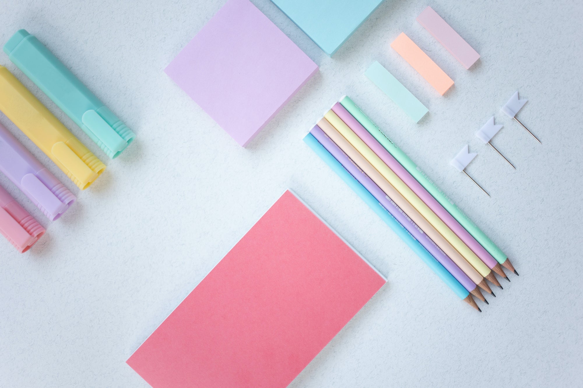 Pastel color bullet journal supplies on a white table like pencils, highlighters, post its, flags and colored paper.